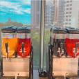 Two juice dispensers on a table in front of a window, offering *240 Drinks* for Slushie Machine Hire.