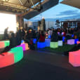 A group of people sitting on a bench in front of a Glow Cube Hire screen.