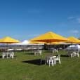 A group of tables and chairs on a grassy field with yellow umbrellas, enhanced by the addition of a 3mx3m Pop Up Marquee With White Roof.