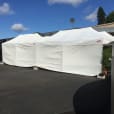 A white 3mx6m pop up marquee with walls on 3 sides is set up in front of a building.