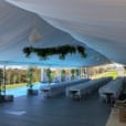 A white tent set up with tables and chairs illuminated by white pendant rope light.