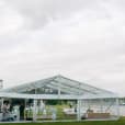 An elegant framed marquee, measuring 8m x 42m, set up on a grassy area near the water for a beautiful wedding celebration.