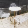 A set of white stools and a gold wire arrow table on a patio.