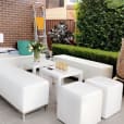 A patio with white furniture, including a white ottoman cube hire, and potted plants.