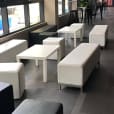 A group of white couches and tables in a lobby, accented with a black ottoman.