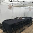 A table set up in a white tent with black chairs and a black tablecloth.