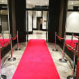 A red carpet leading into a building, flanked by sleek chrome bollards.