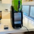 A green juice machine *sitting on a counter* in a kitchen.