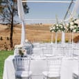 A wedding reception set up in a field with tables and white chairs hired from Clear Tiffany Chair Hire.