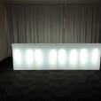 A straight white LED bar in a room with curtains, designed to glow.