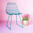 A turquoise blue chair with a potted plant on a pink background.