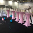 Pink balloons and tables in a room with a white picket fence, equipped with a stainless steel cocktail bar table.