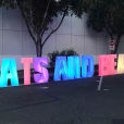 A sign with glow letters that says "eats and beats" in front of a parking lot.