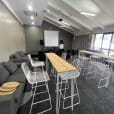 A room with white hairpin high bar tables and chairs with timber tops, and a projector.