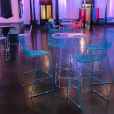 A room with turquoise wire stools and chairs in a dark room.