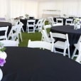 A white tent with black tables and chairs adorned with black round banquet tablecloths.