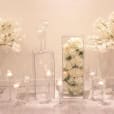 Clear vases with white flowers and candles in them.