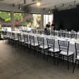 A long table set up with black Tiffany chairs and white tablecloths.