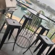 A black wire cocktail table with stools and a grill on a balcony overlooking the water.