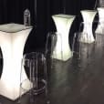 Clear ghost stools placed around lighted bar tables in a room.