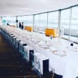 A long white table with white chairs and a view of the harbour.