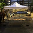 A white tent with tables and chairs in the middle of a city, featuring Timber Trestle Table 2.4m Hire setup.