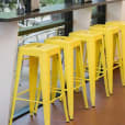 Yellow Tolix Stool Hire - A row of yellow bar stools in front of a window.