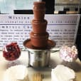 A medium commercial chocolate fountain on a table in a conference room.