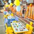 A colorful table set up in a warehouse adorned with vibrant balloons and whimsical tablecloths.