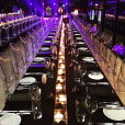 A large trestle table is set up in a dark room with candles, covered by a black tablecloth.