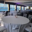 A room with white tables and chairs, adorned with white round banquet tablecloth hire, offering a stunning view of the ocean.