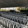 A large tent with rows of white plastic stackable chairs.