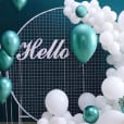 A white and green balloon arch with the word hello displayed on a circular mesh backdrop.