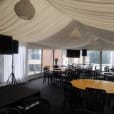 A white tent with tables and chairs in it illuminated by white pendant rope lights.