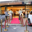 A red carpet leading to a car in a parking lot adorned with gold bollards.