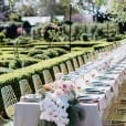 A long table set up in a garden with gold wire chairs.