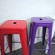 A row of colorful metal stools, including purple Tolix stools, in a room.