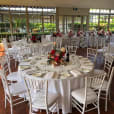 A room with white round banquet tables and chairs set up for a wedding.