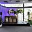 A room adorned with flowers and plants featuring a PA system with wireless mic and speaker stands.