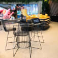 The interior of a coffee shop with black stools and plants, featuring black wire cocktail table hire.