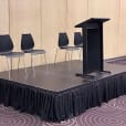 A podium stand with four black executive chairs.