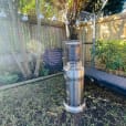 A stainless steel barbecue in a backyard, featuring Pkg 2 - 2 x Area Heater Hire w/ Gas Bottles for added convenience and comfort.