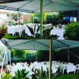 A white tent with tables and chairs set up in a garden, illuminated with LED floodlights.