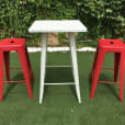 Two red Tolix stools and a table in a grassy area.