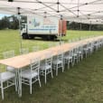 A long gold hairpin banquet table with white chairs, set under a tent.