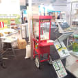A man standing next to a popcorn cart at a trade show.