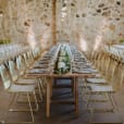 A wedding reception set up in a stone barn with gold wire chairs.