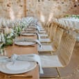 A table set up with white linens and greenery, accentuated by elegant gold wire chairs.