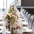 A long table set with clear Victorian ghost chairs and adorned with beautiful flowers.