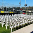 A large group of white plastic chairs on a grass field.